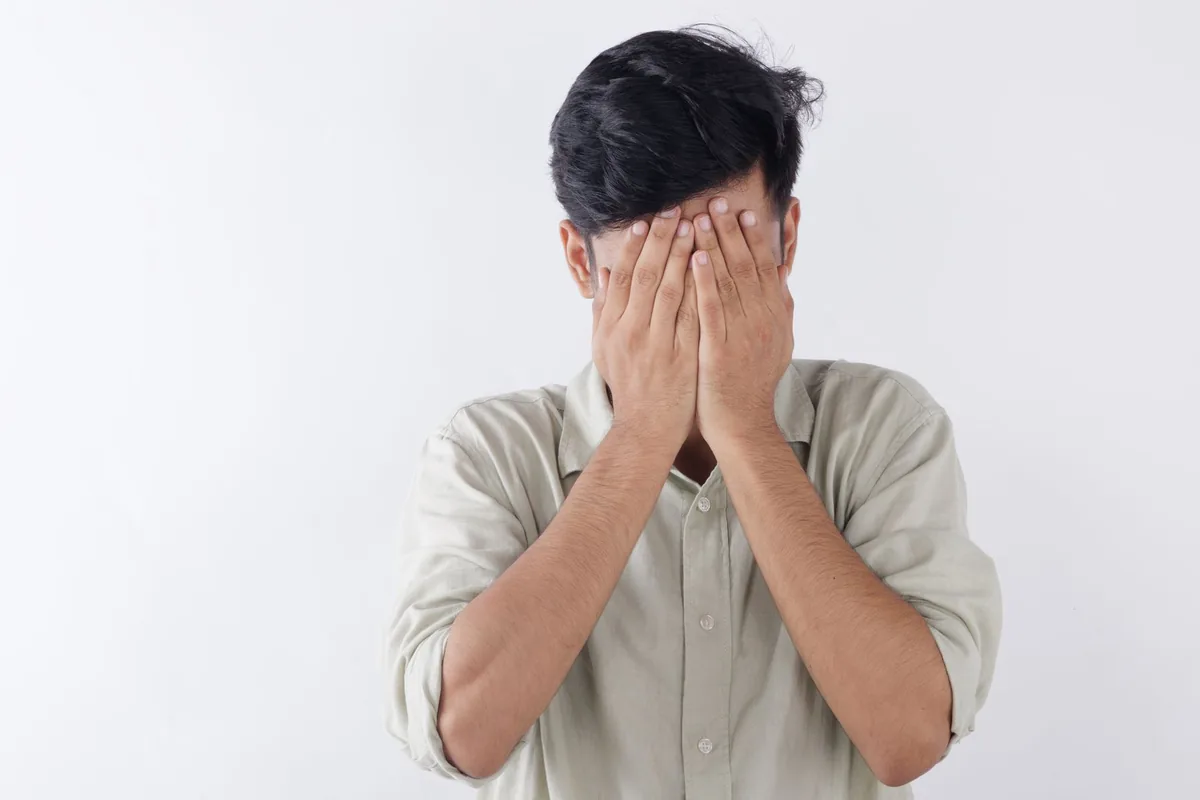A man covering his face with his hands in distress.