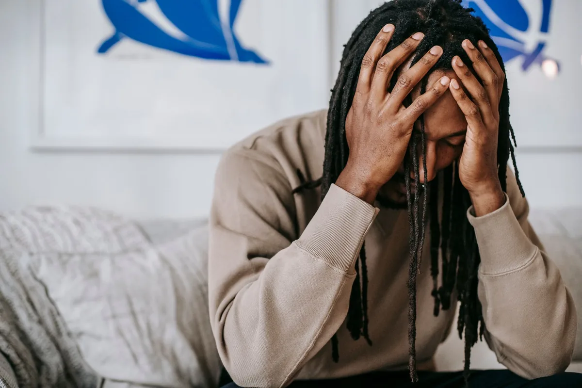 An anxious man holding his head, eyes closed.