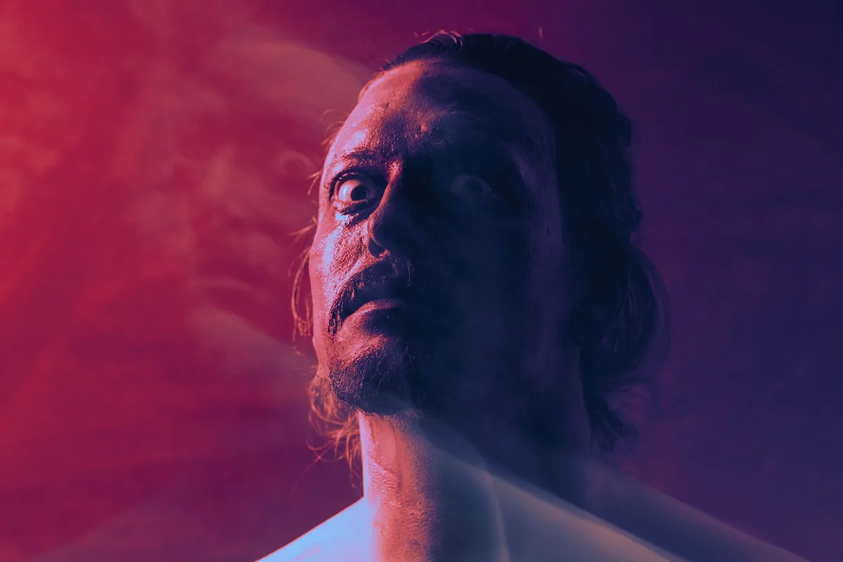 A man with a frightened, fearful expression under dramatic lighting.