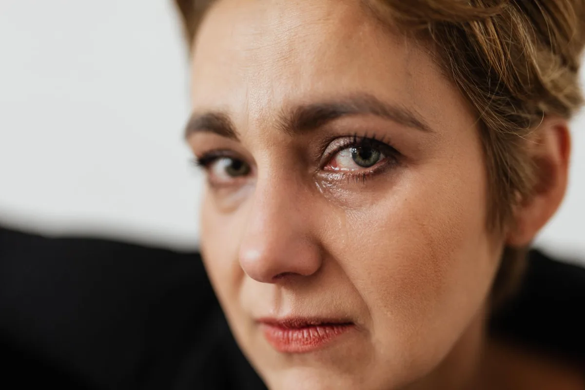A close-up of a woman with tearful eyes, looking sad.