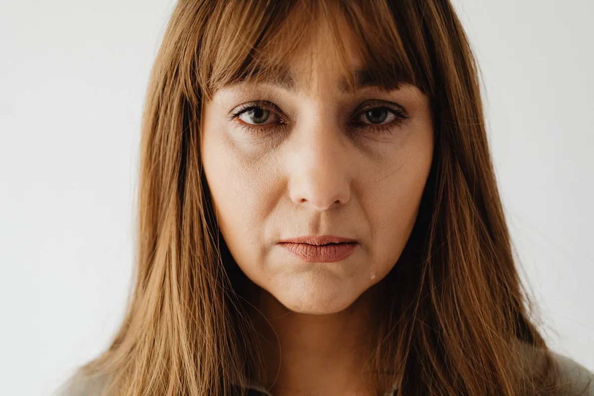 A woman with tears in her eyes, looking downcast.